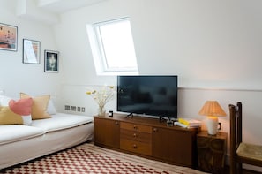 Ein Schlafzimmer mit einem Bett, einem Fernseher auf einer Holzkommode, einem Fenster und einer Lampe.