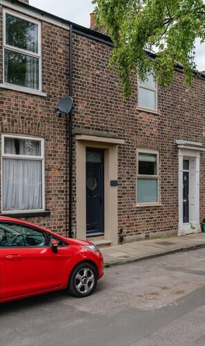 A red car parked in front of a brick house with a black door and a satellite dish. - Swan House 3-bed Town House York - up to 5 Guests (York)