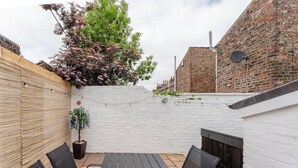 A rooftop patio with a black table and chairs, a white brick wall, and a tree with pink flowers. - Swan House 3-bed Town House York - up to 5 Guests (York)