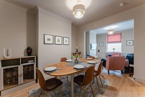 A dining area with a wooden table, chairs, and a chandelier. There are framed pictures on the wall and a window with a view. - Swan House 3-bed Town House York - up to 5 Guests (York)