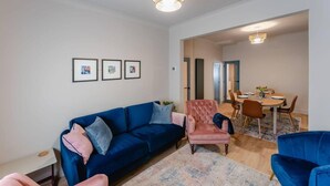 A living room with a blue sofa, a pink armchair, and a dining area with a table and chairs. - Swan House 3-bed Town House York - up to 5 Guests (York)