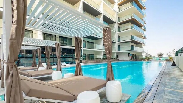 A swimming pool with lounge chairs and umbrellas, surrounded by a modern building with balconies.