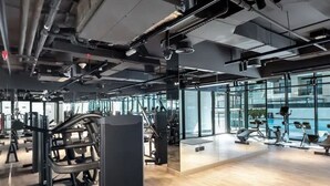 A modern gym with various exercise equipment, large windows, and a wooden floor.