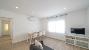 Una sala de estar moderna con comedor, televisor de pantalla plana y un ventanal con cortinas.