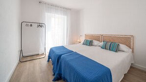Un dormitorio con una cama grande, dos almohadas, una mesita de noche con lámpara y un perchero.