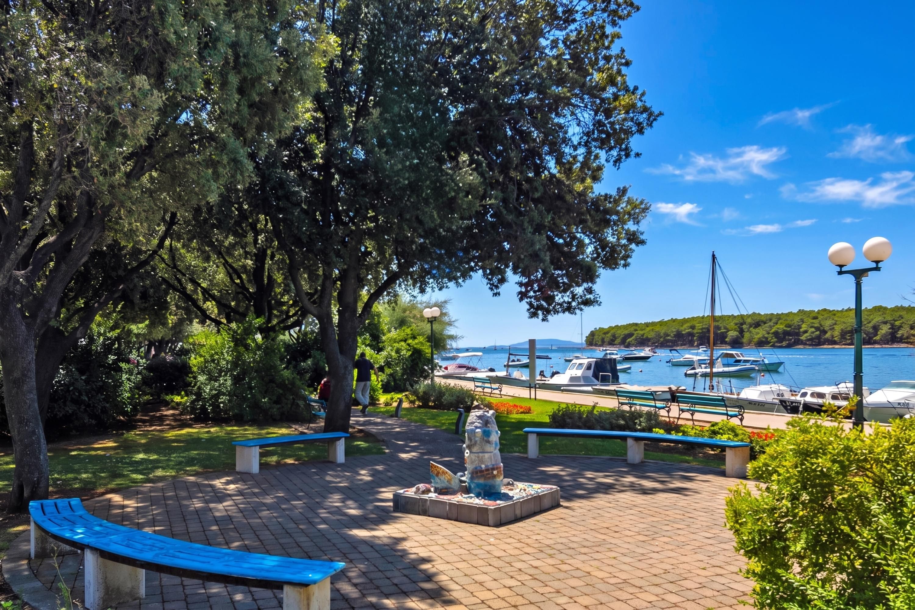 A park with benches, a statue, and a view of boats on the water.