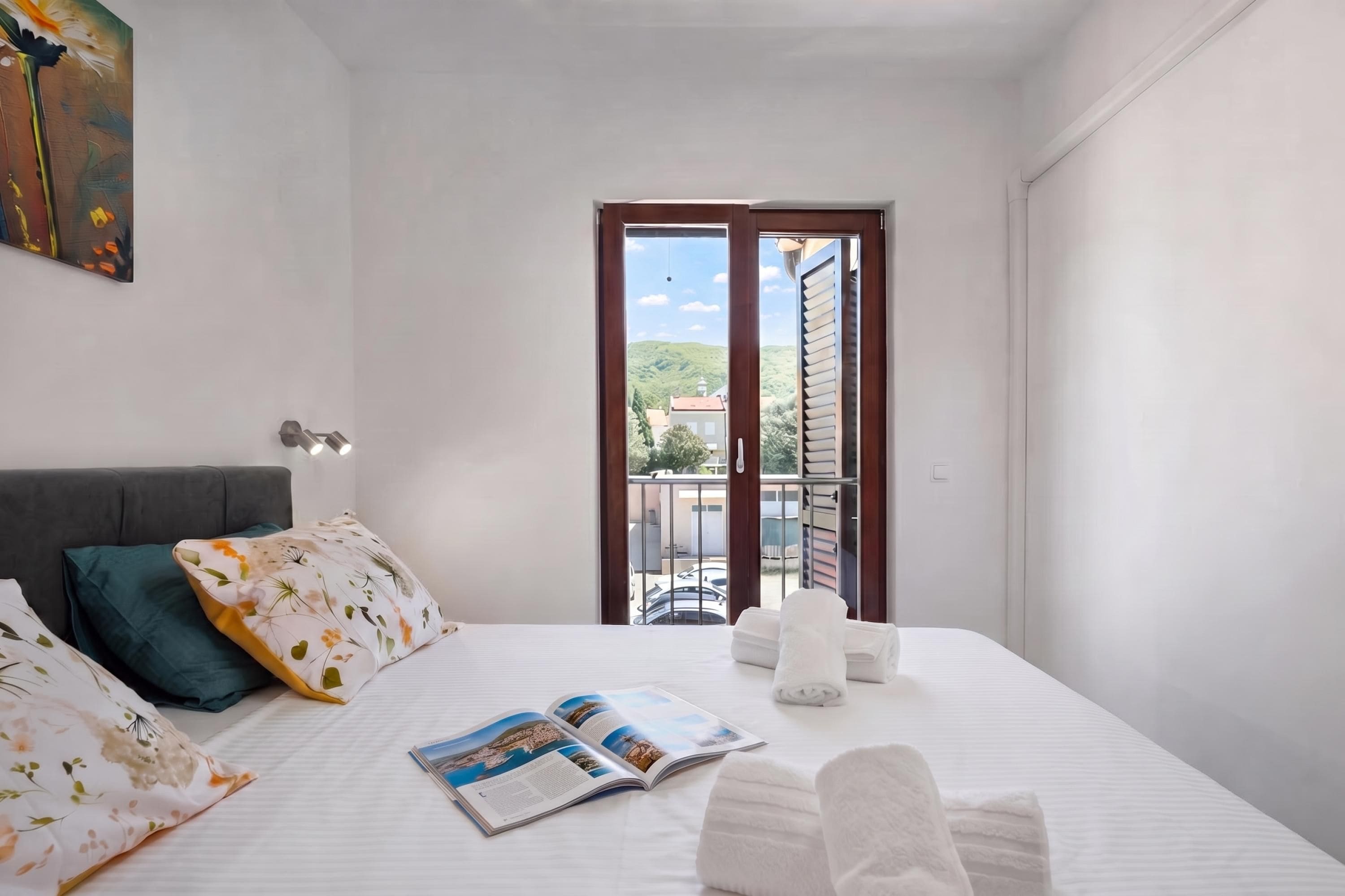 A hotel room with a bed, pillows, a magazine, and a view of the outside.