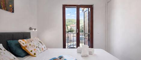 A hotel room with a bed, pillows, a magazine, and a view of the outside.