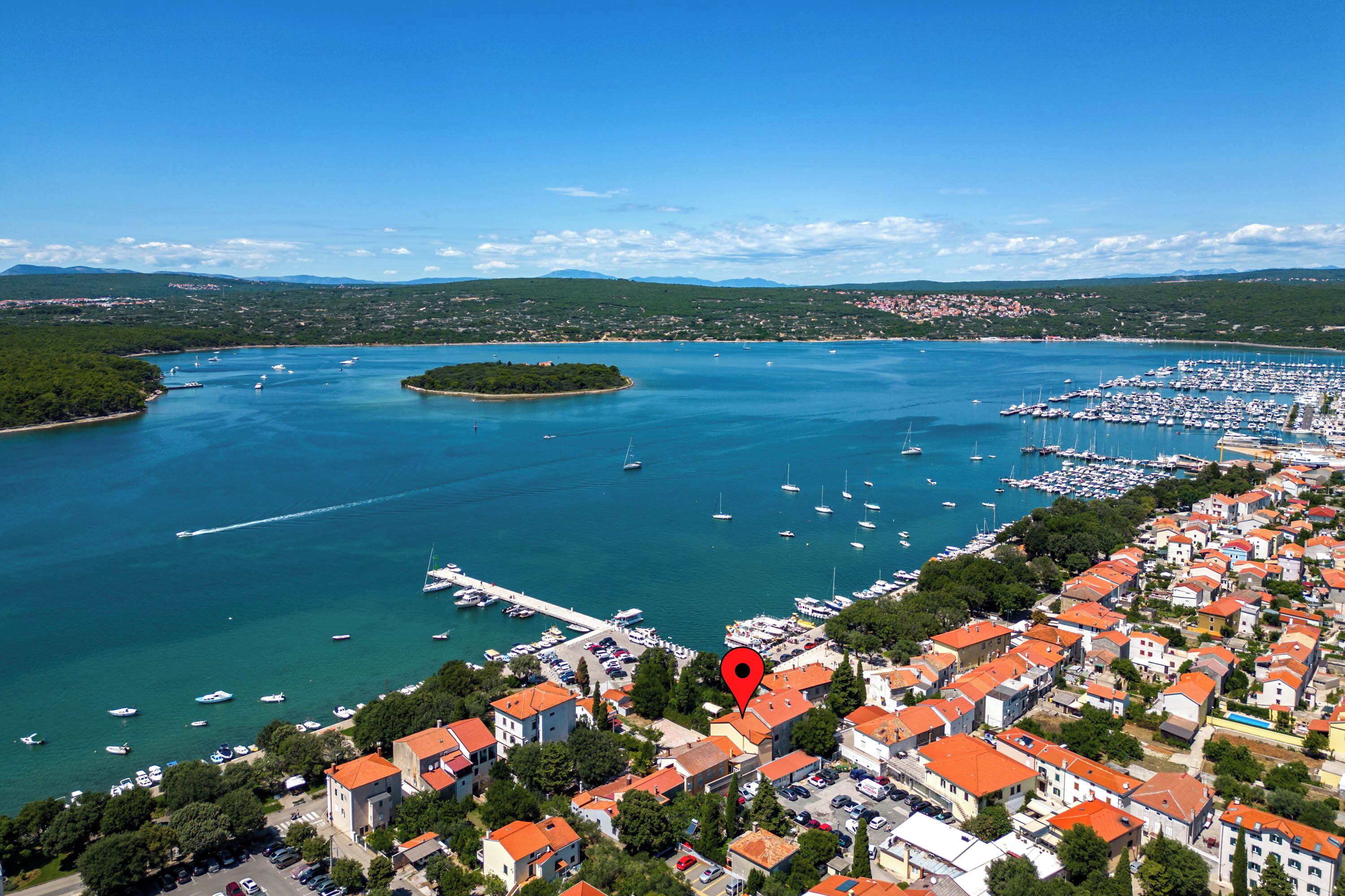 An aerial view of a coastal town with a marina, boats, and buildings with red-tiled roofs.