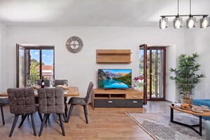A modern living room with a dining area, a TV on the wall, and a large window.