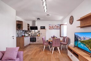 A modern kitchen with a flat-screen TV, dining area with chairs, and a large window. - Seafront Apartment Nana (Punat)