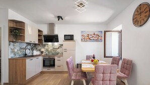 A modern kitchen with wooden cabinets, a marble backsplash, and a dining area with pink upholstered chairs and a wooden table. - Seafront Apartment Nana 2 (Punat)