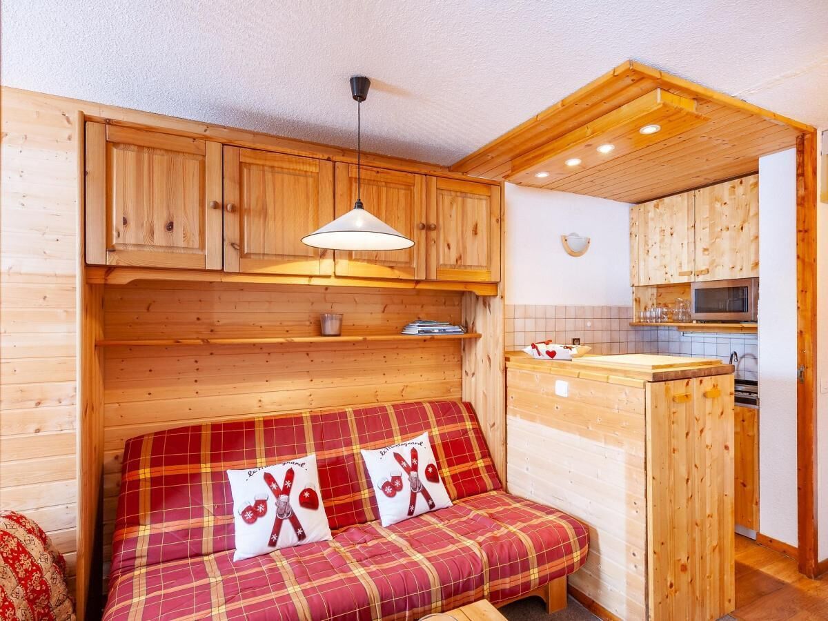 A cozy cabin-style room with a wooden sofa, a hanging light fixture, and a kitchen area with a microwave.