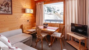 Une pièce chaleureuse avec des murs en bois, un canapé, une table à manger avec des chaises, un téléviseur et une fenêtre avec des rideaux.