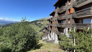 Un immeuble en bois à plusieurs étages, doté de balcons, qui se dresse sur un fond de paysage montagneux.