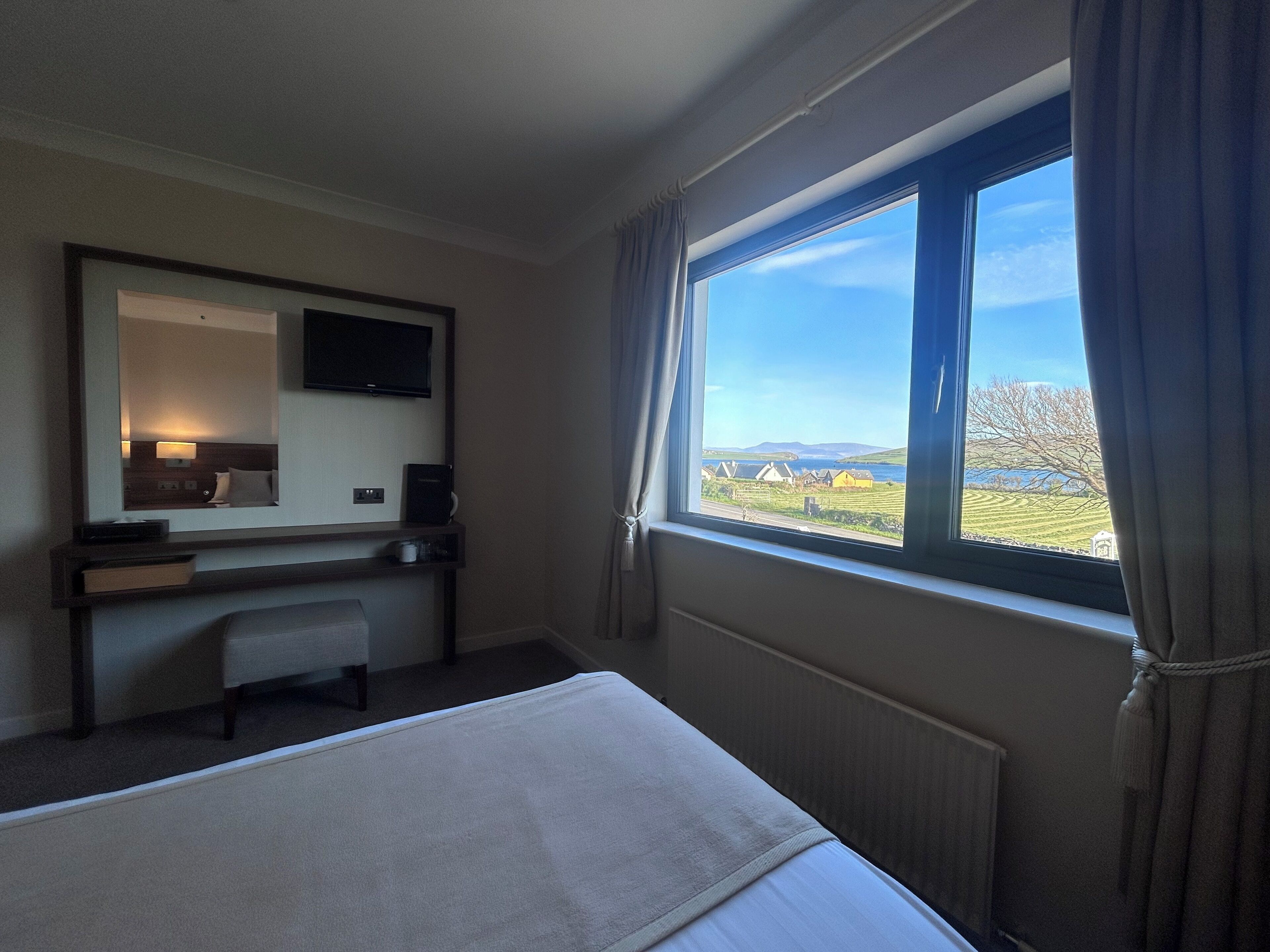 Ein Hotelzimmer mit Bett, Schreibtisch, Stuhl, Fernseher und einem Fenster mit Blick auf die Landschaft.