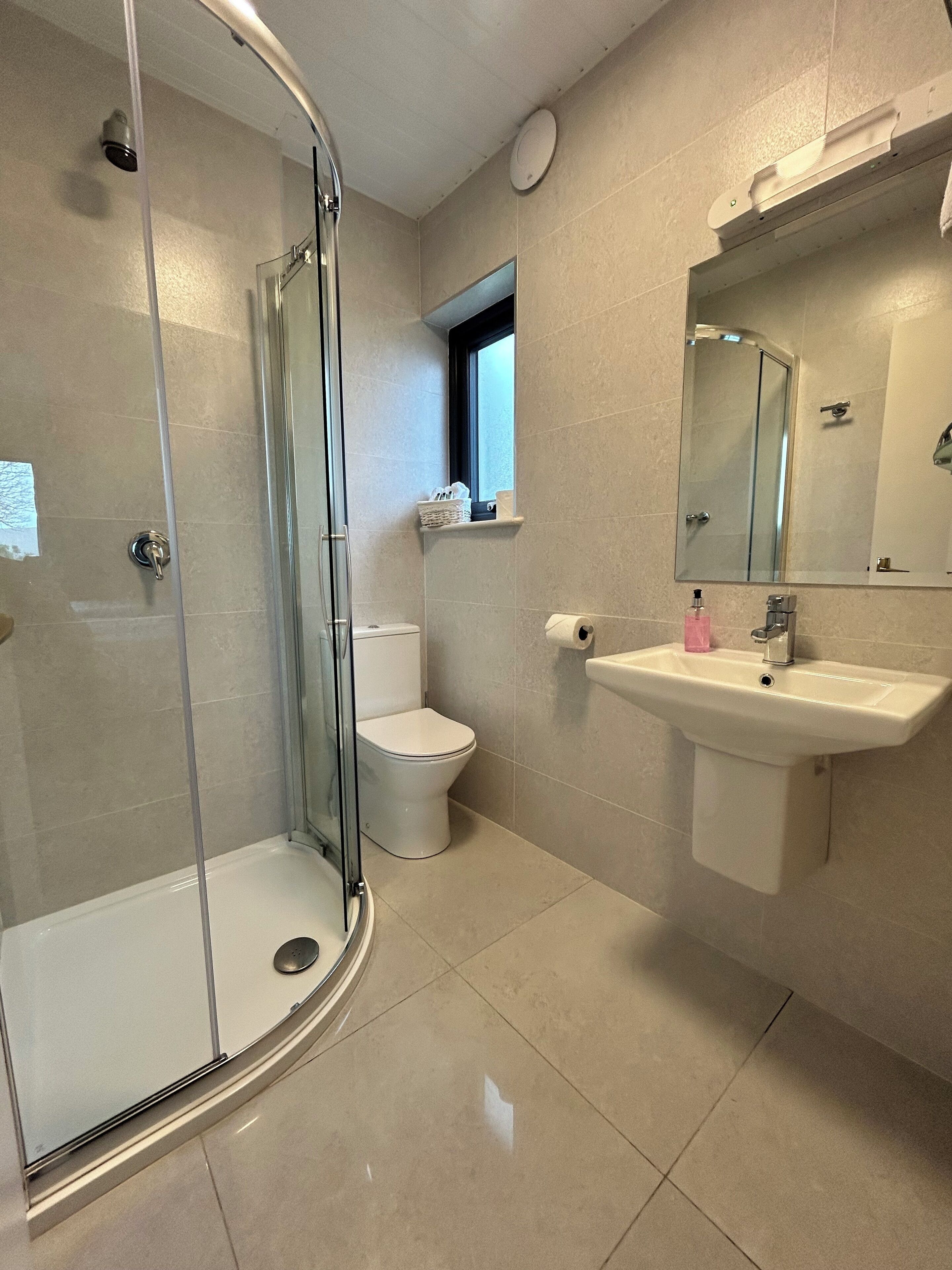Un baño moderno con ducha de vidrio, inodoro y lavamanos con espejo.