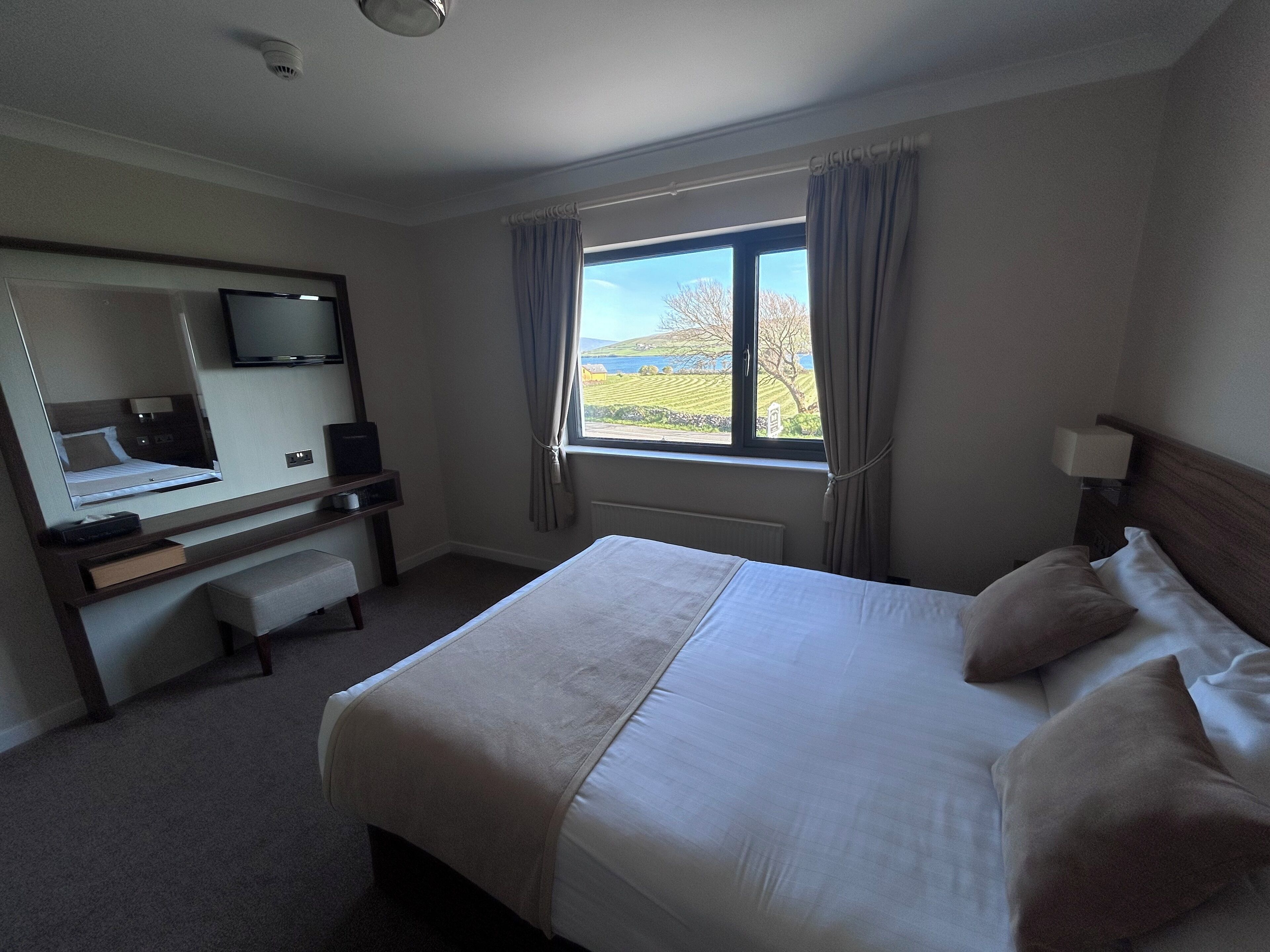 A hotel room with a bed, a desk with a chair, a television, and a window with curtains.