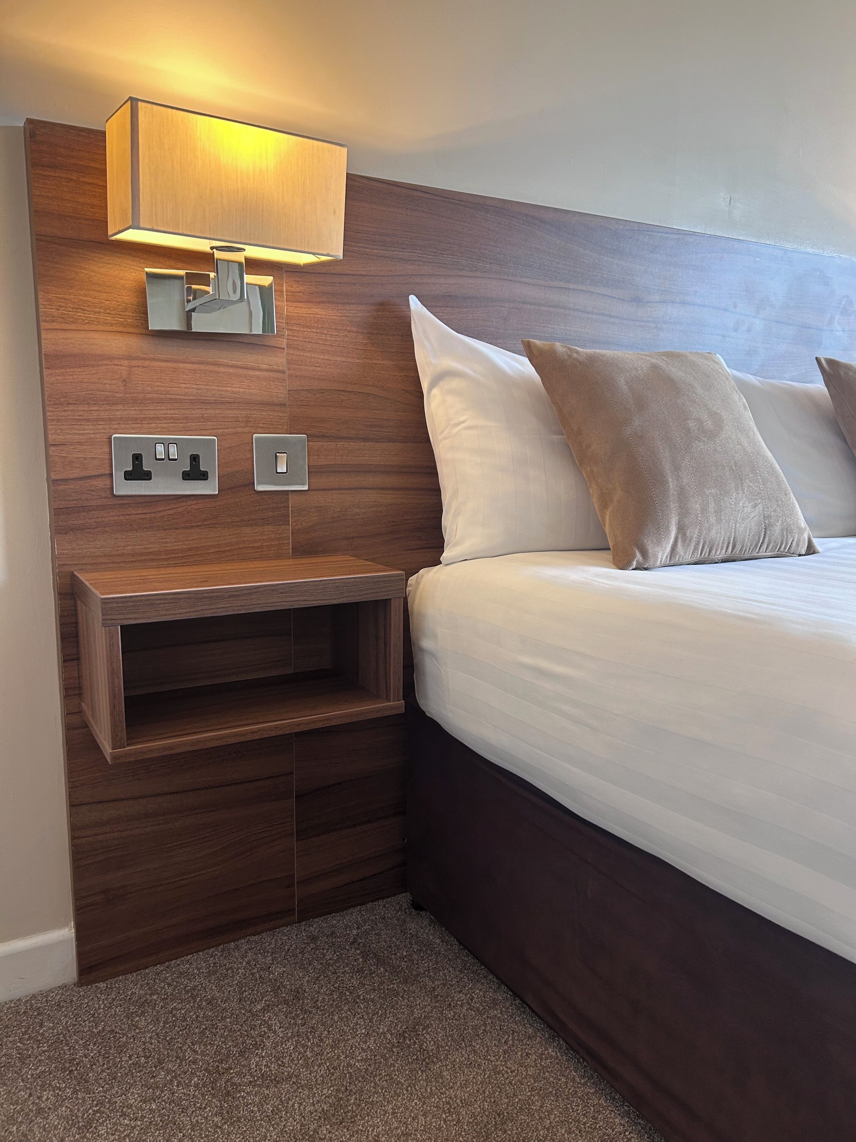 Une chambre à coucher moderne avec une tête de lit en bois, une table de chevet avec une lampe et un lit avec des oreillers.