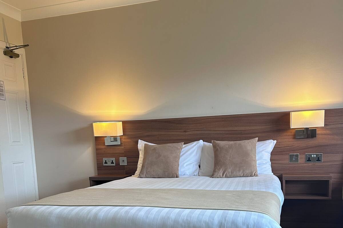 A large bed with a wooden headboard, two bedside lamps, and a neutral-colored carpet.