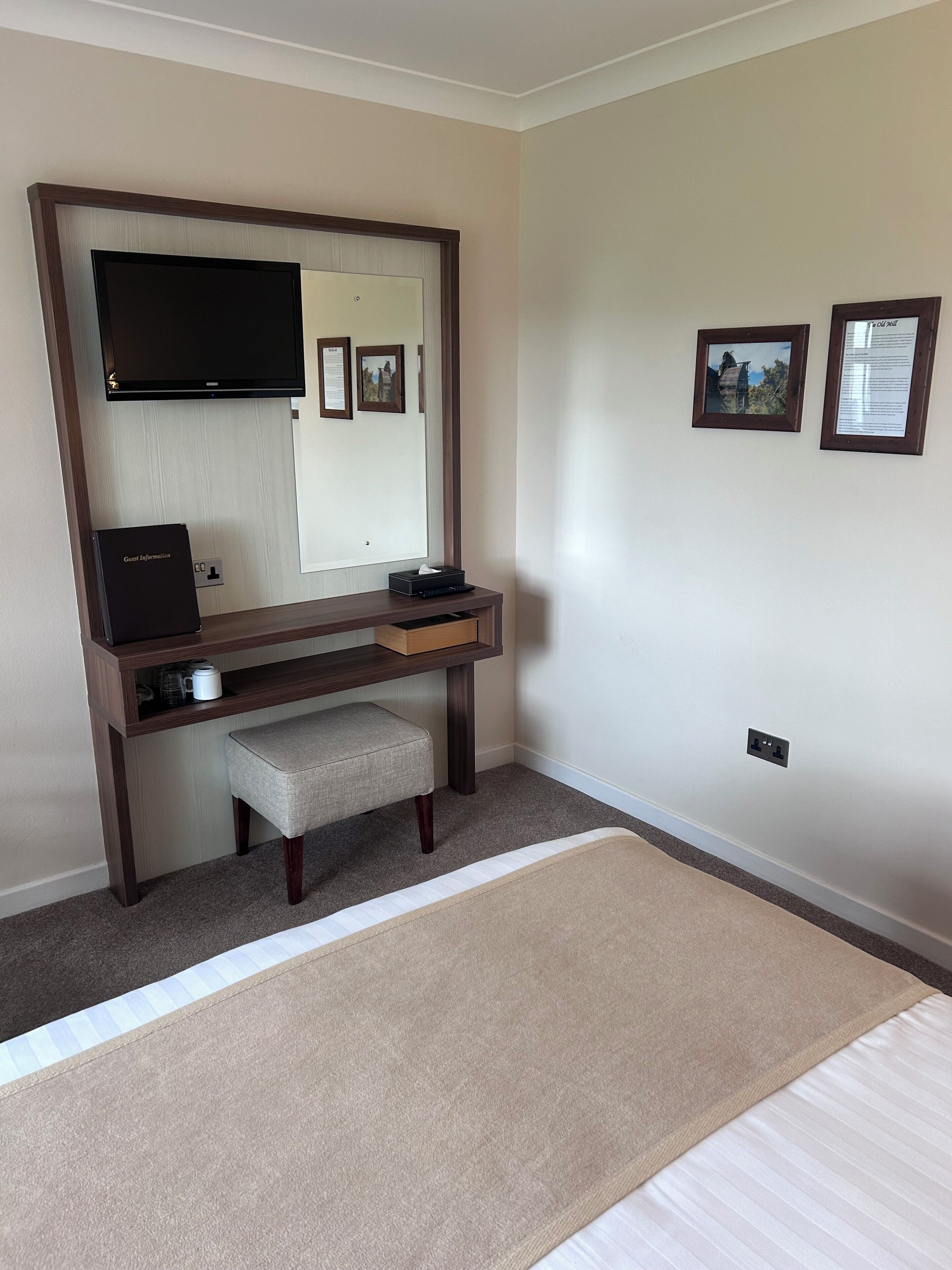 A hotel room with a bed, a desk with a computer, a chair, a television, and framed pictures on the wall.