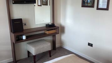 A hotel room with a bed, a desk with a computer, a chair, a television, and framed pictures on the wall.