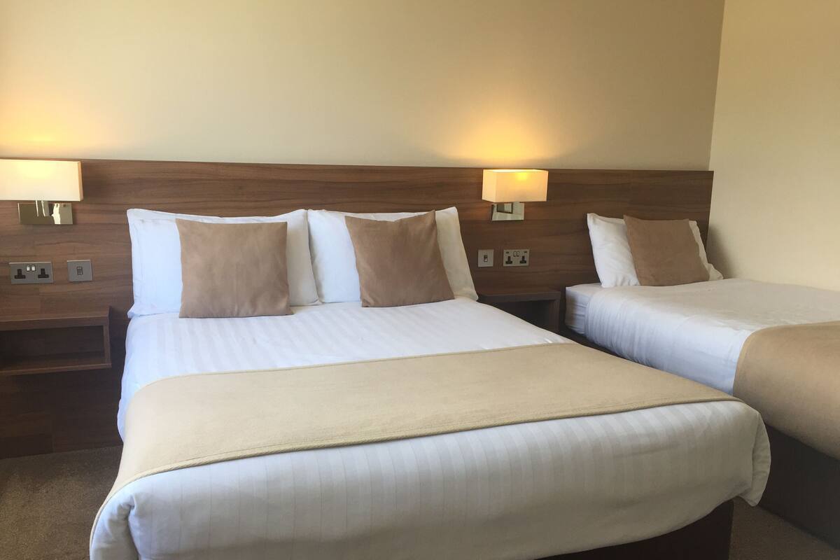 A hotel room with two single beds, each with a headboard, bedside tables, and lamps.