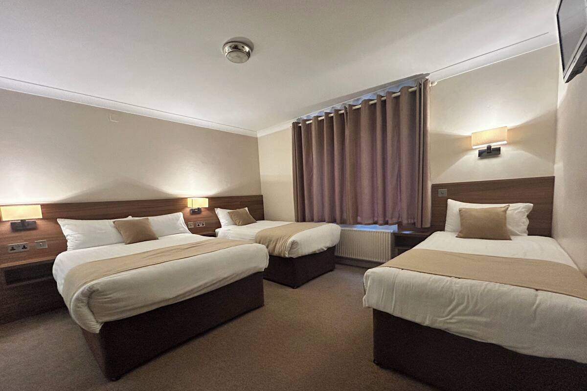 A hotel room with two beds, a nightstand, a lamp, a window with curtains, and a ceiling light.