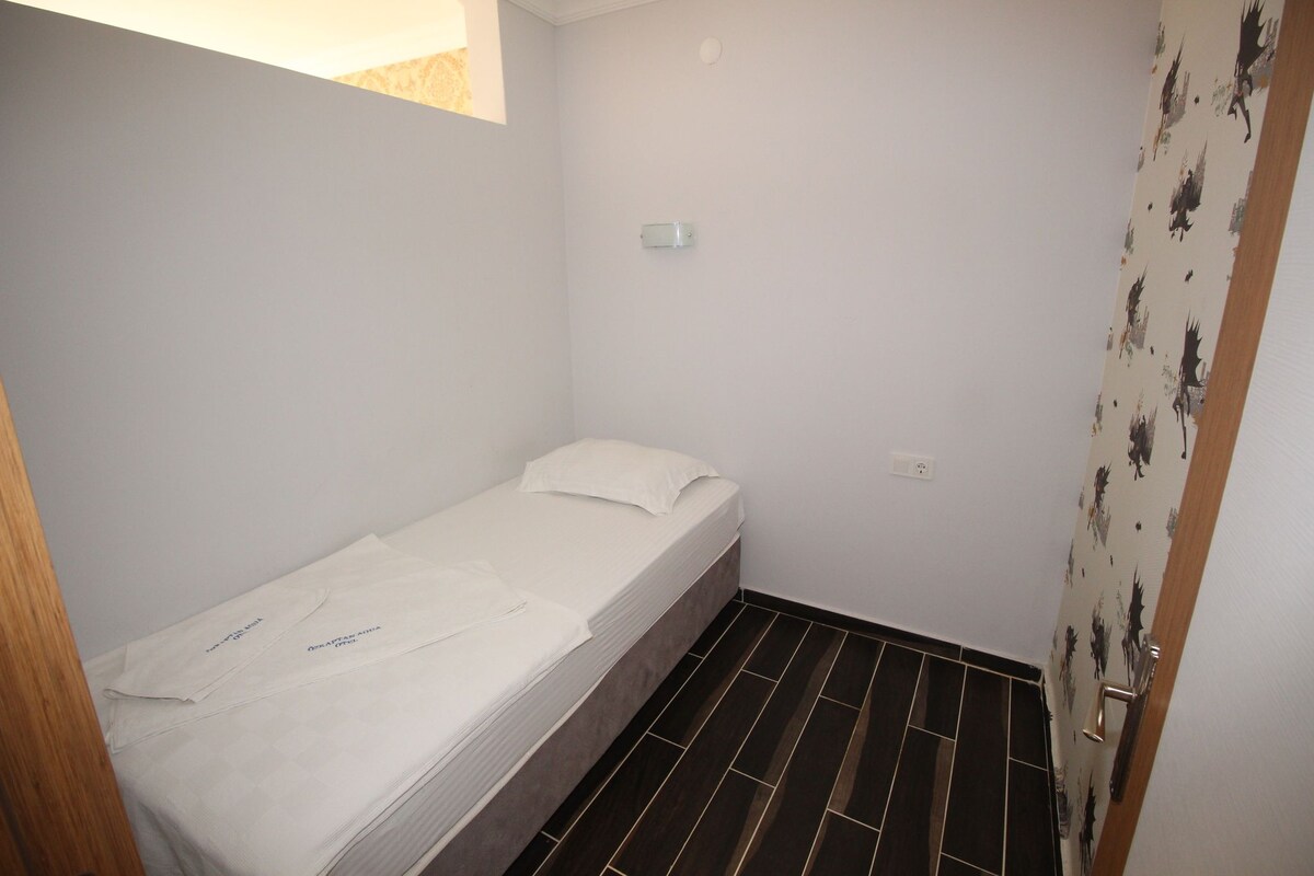 Una habitación pequeña con cama individual, pared blanca sencilla, una ventana pequeña y una puerta con estampado floral.