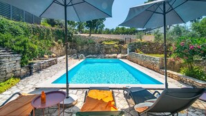A swimming pool with stone walls, surrounded by lounge chairs and umbrellas, set in a garden with stone steps and greenery. - Villa Giovanna (Rakalj)