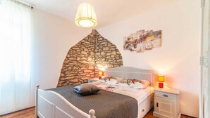 A bedroom with a stone wall, a bed with a headboard, bedside tables with lamps, and a wall-mounted artwork. - Villa Giovanna (Rakalj)