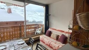 Una habitación con una mesa de comedor lista para cuatro personas, un sofá con cojines, un amplio ventanal con vistas a montañas nevadas y una lámpara de techo.