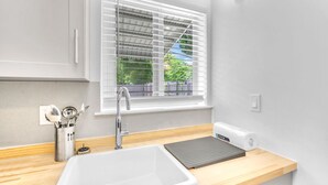 Eine moderne Küche mit einem weißen Spülbecken, einem Besteckhalter aus Edelstahl und einem Fenster mit Jalousien.
