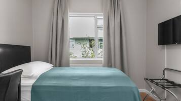 A hotel room with a bed, a chair, a TV, and a window with curtains.