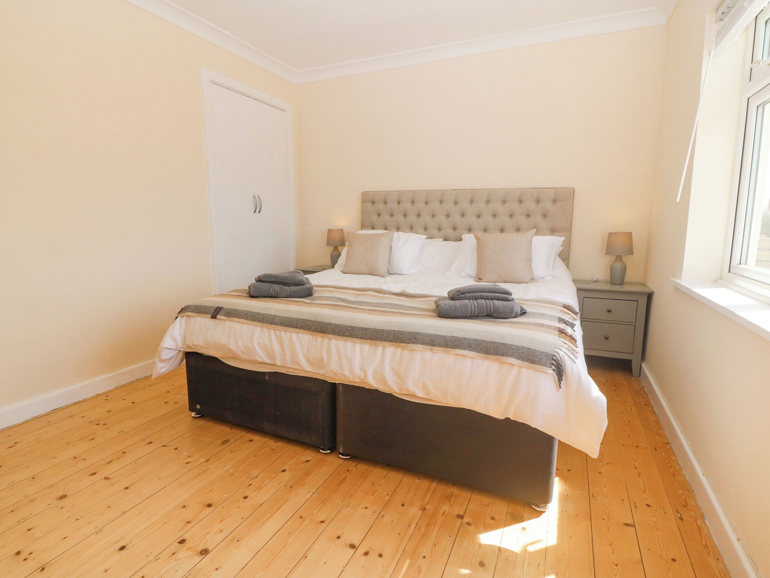 A bedroom with a large bed, a nightstand, a window, and a door.