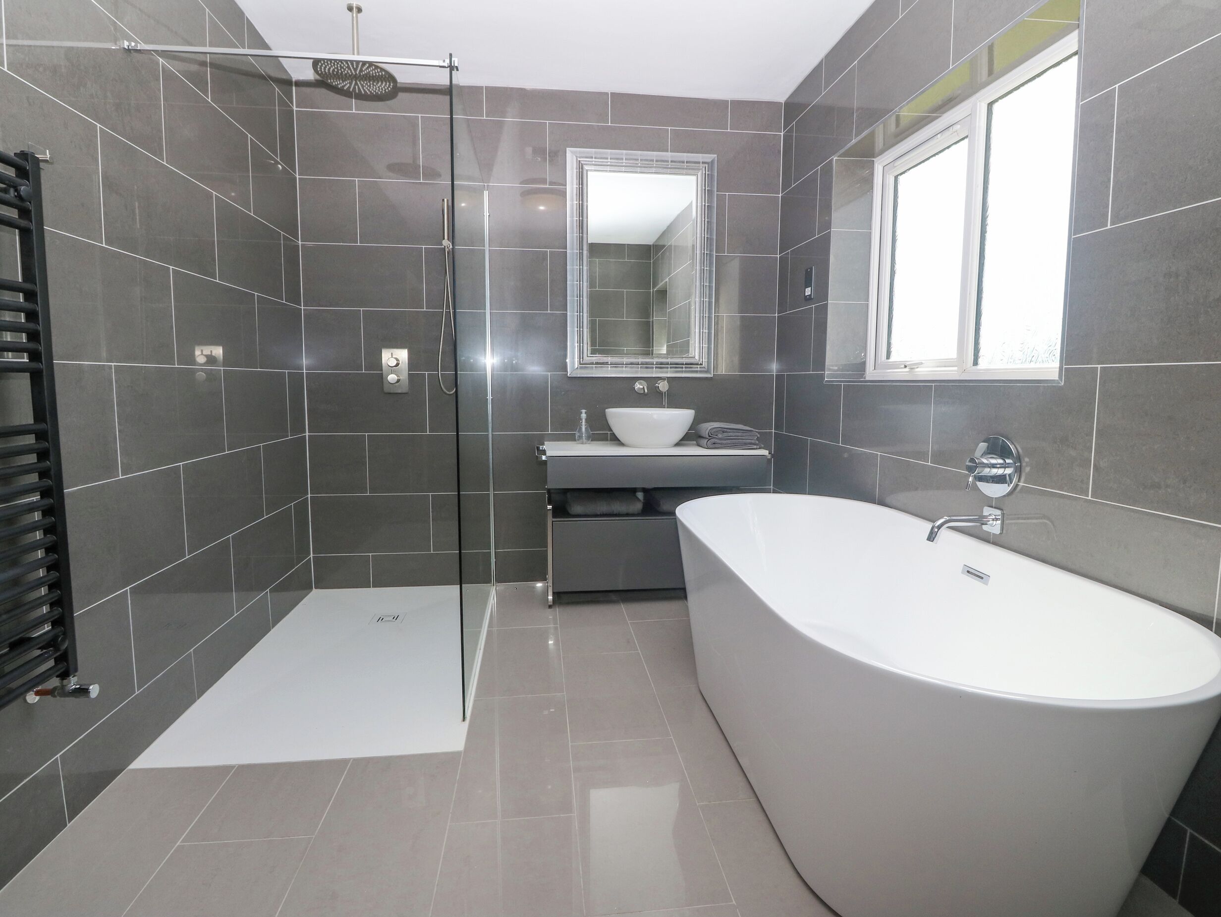 Un baño moderno con cabina de ducha a ras de suelo, bañera independiente y tocador con espejo.
