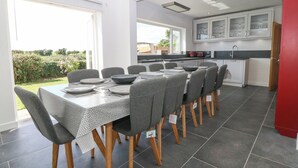 Un coin repas avec une table dressée pour six personnes, une cuisine en arrière-plan et une vue sur le jardin.