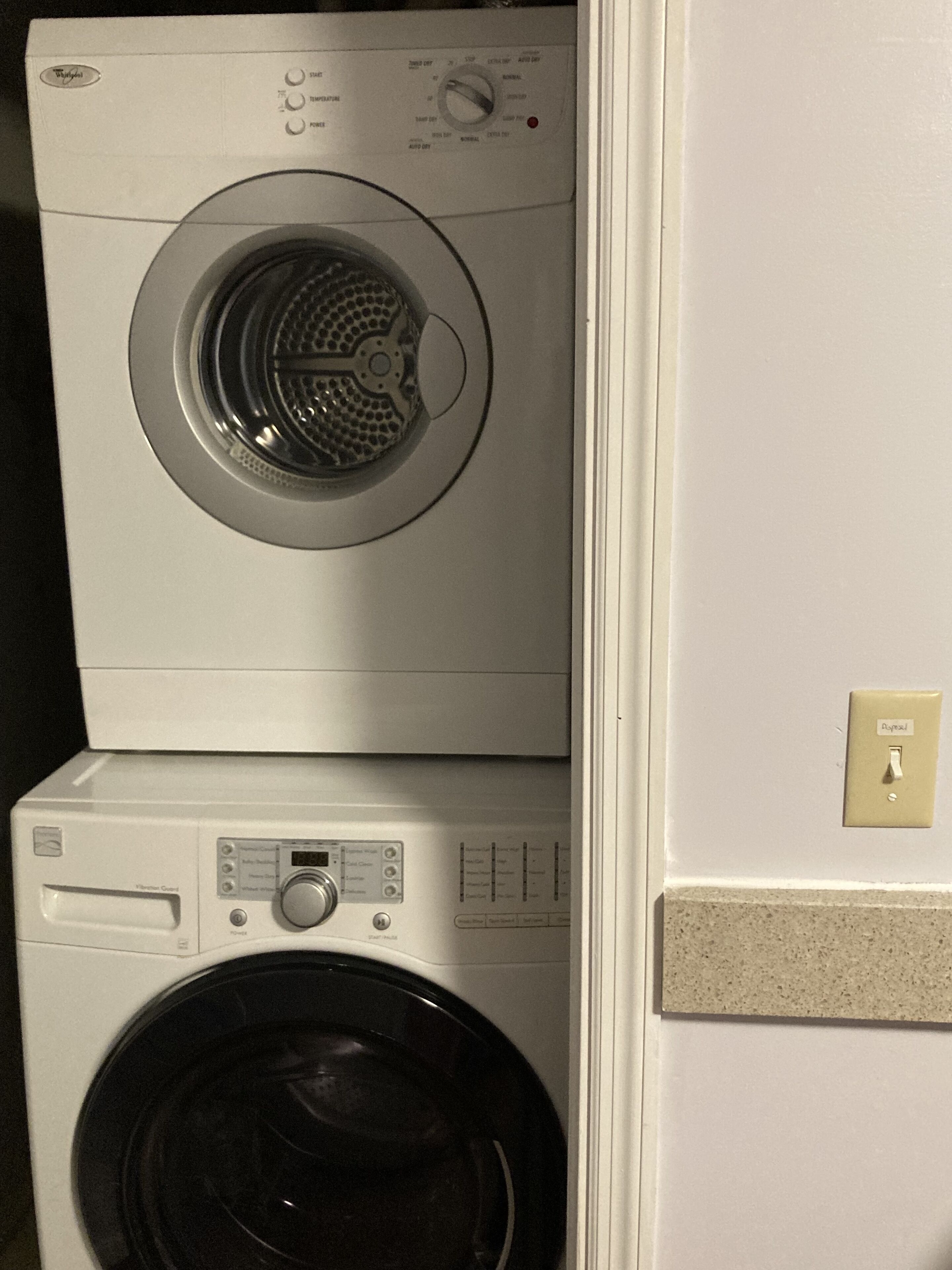 A stacked washer and dryer unit with control panels and a power switch on the wall.