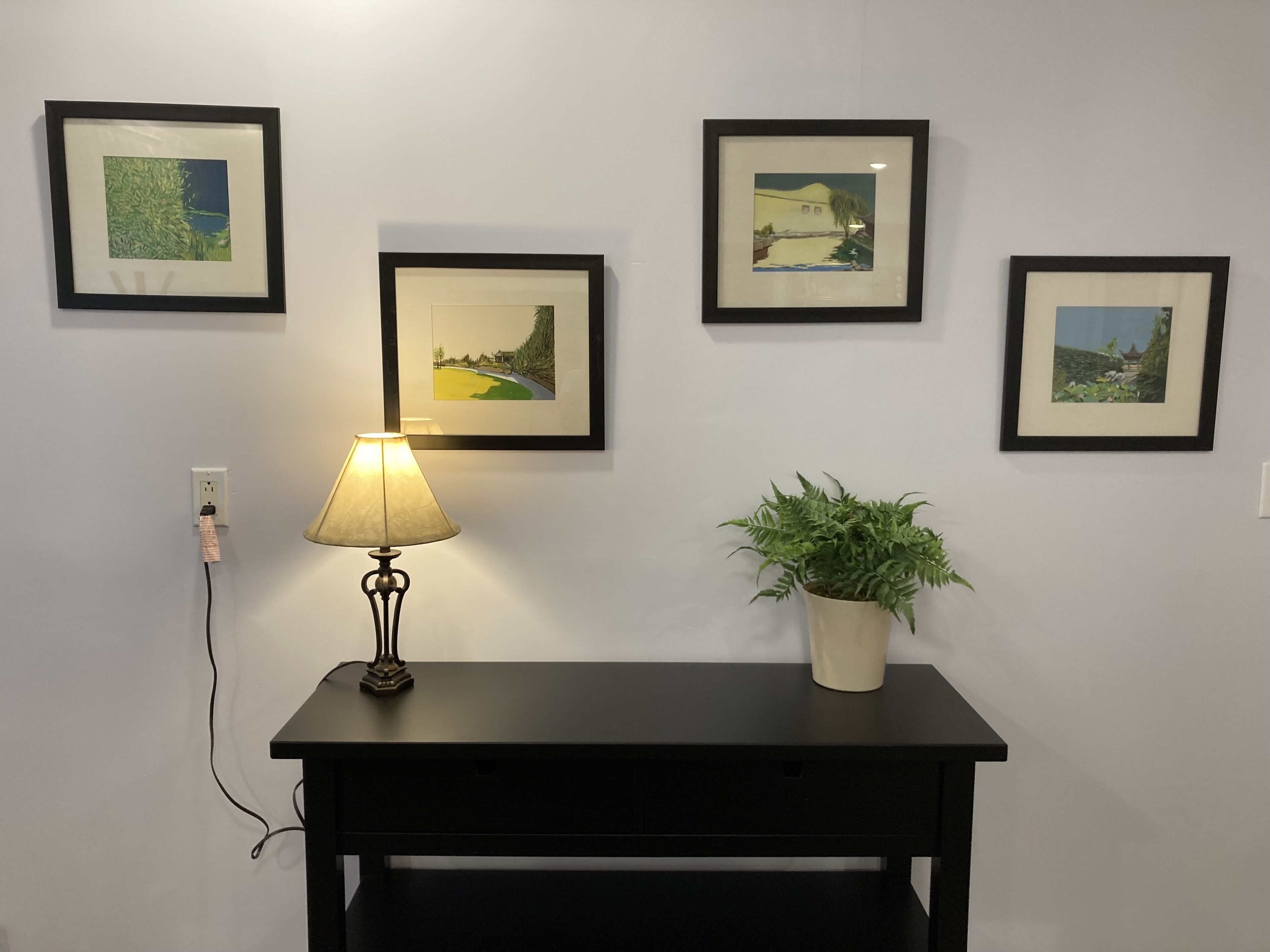 Uma mesa preta com uma luminária e um vaso de planta em frente a uma parede com quatro quadros.