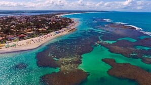 Luchtbeeld van een kustgebied met een strand, helder turquoise water en een rotsachtige kustlijn.