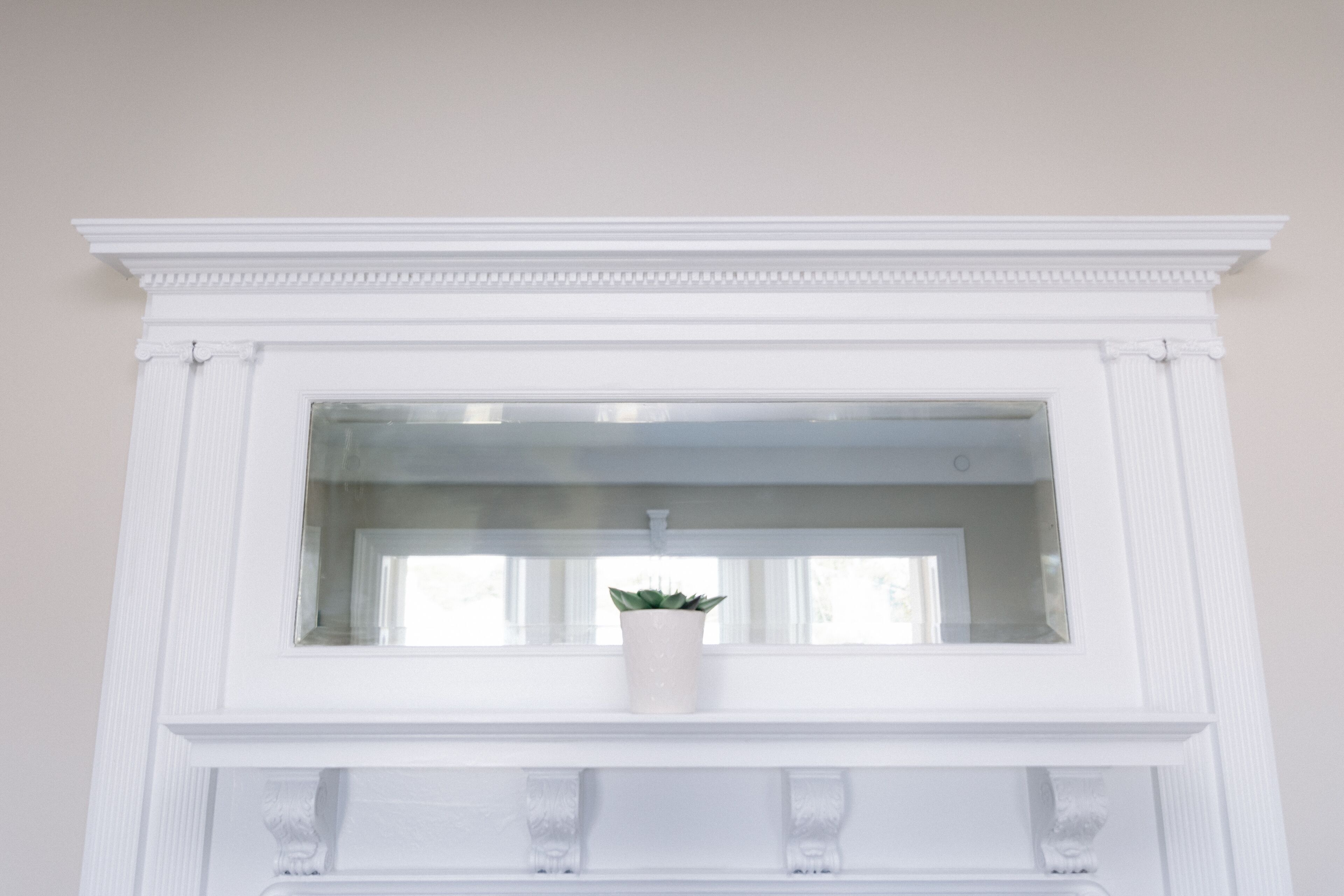 Une cheminée blanche, ornée d’un manteau décoratif, sur lequel est posée une petite plante en pot.