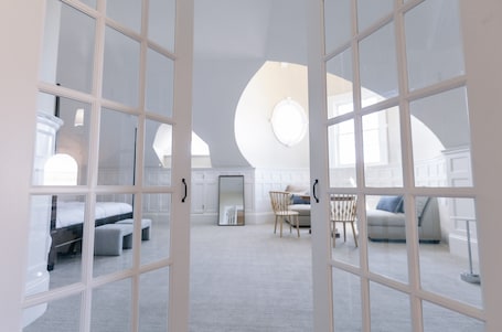 A spacious room with a high ceiling, large windows, and a cozy seating area with a sofa and chairs.