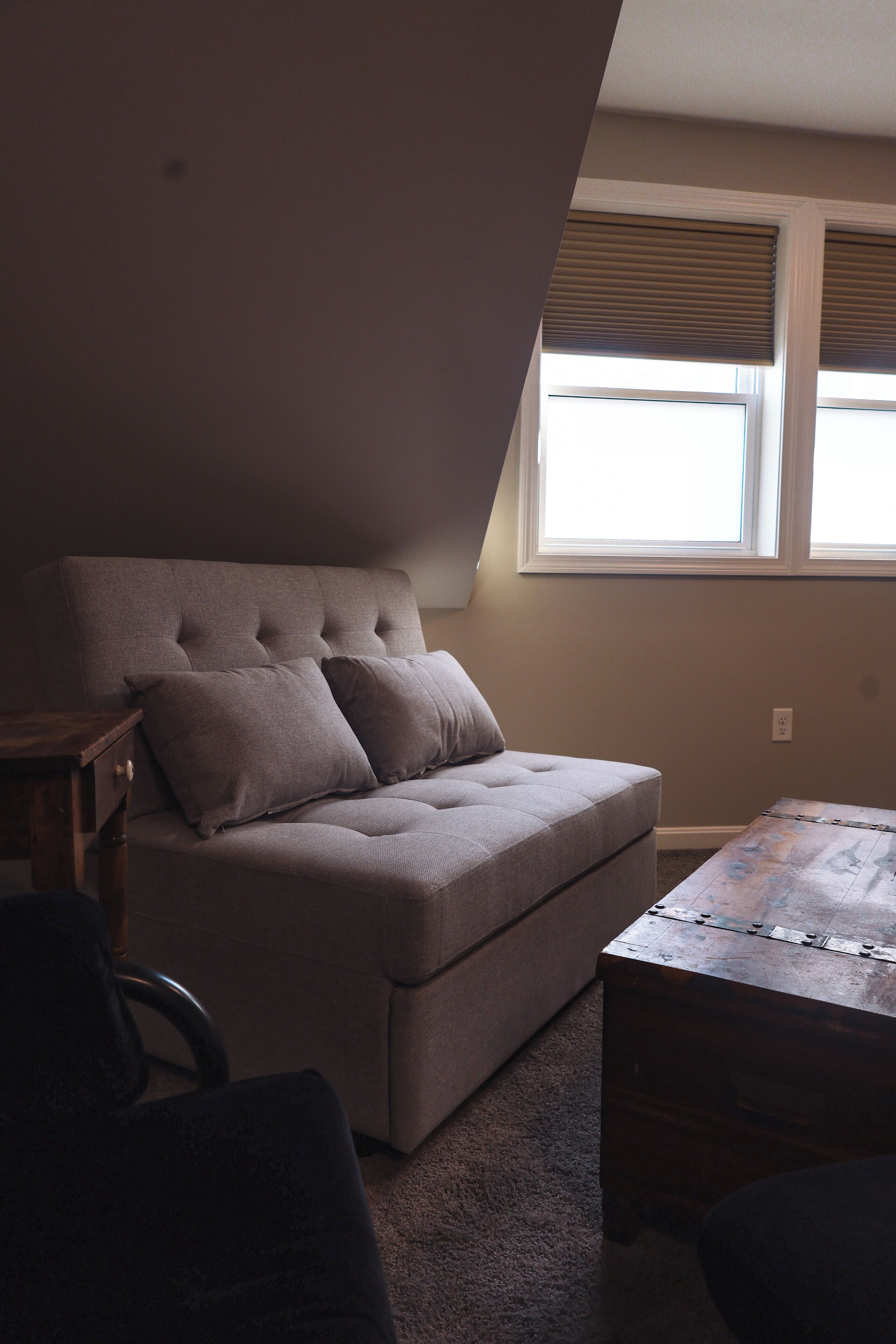 A room with a sofa, a wooden table, and a window with blinds.
