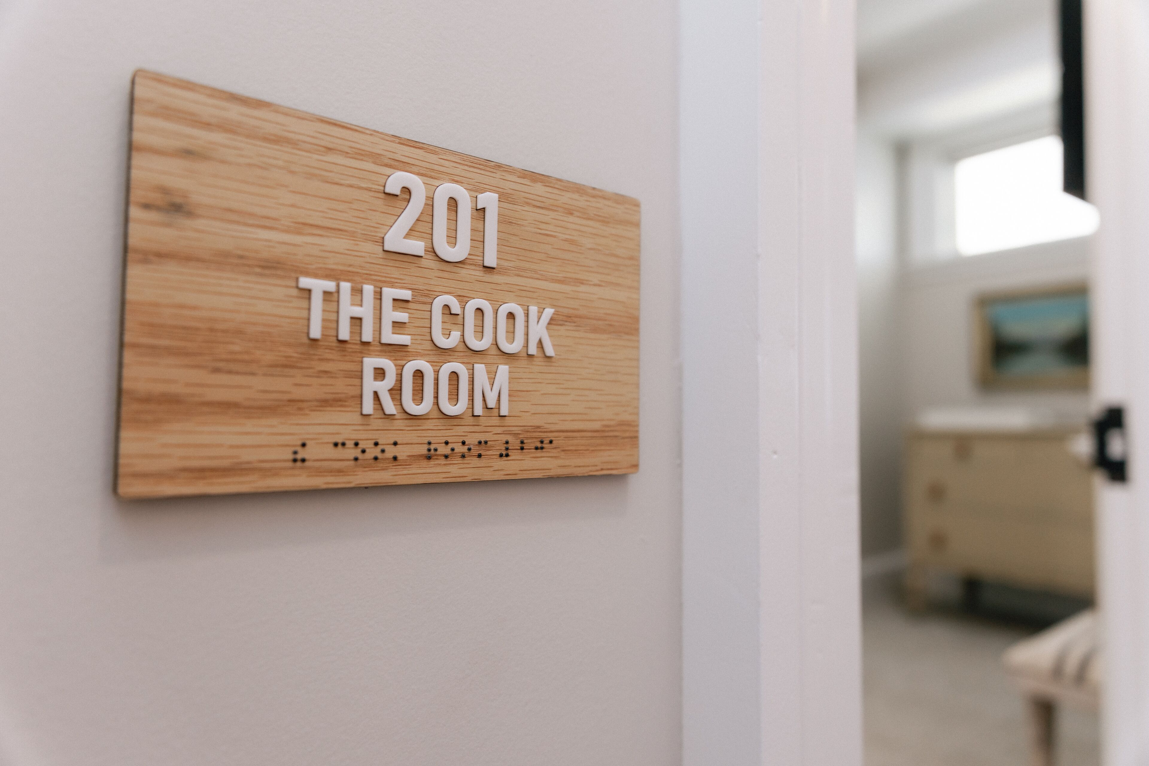 Una señal de madera con el texto "201 THE COOK ROOM" en una pared.