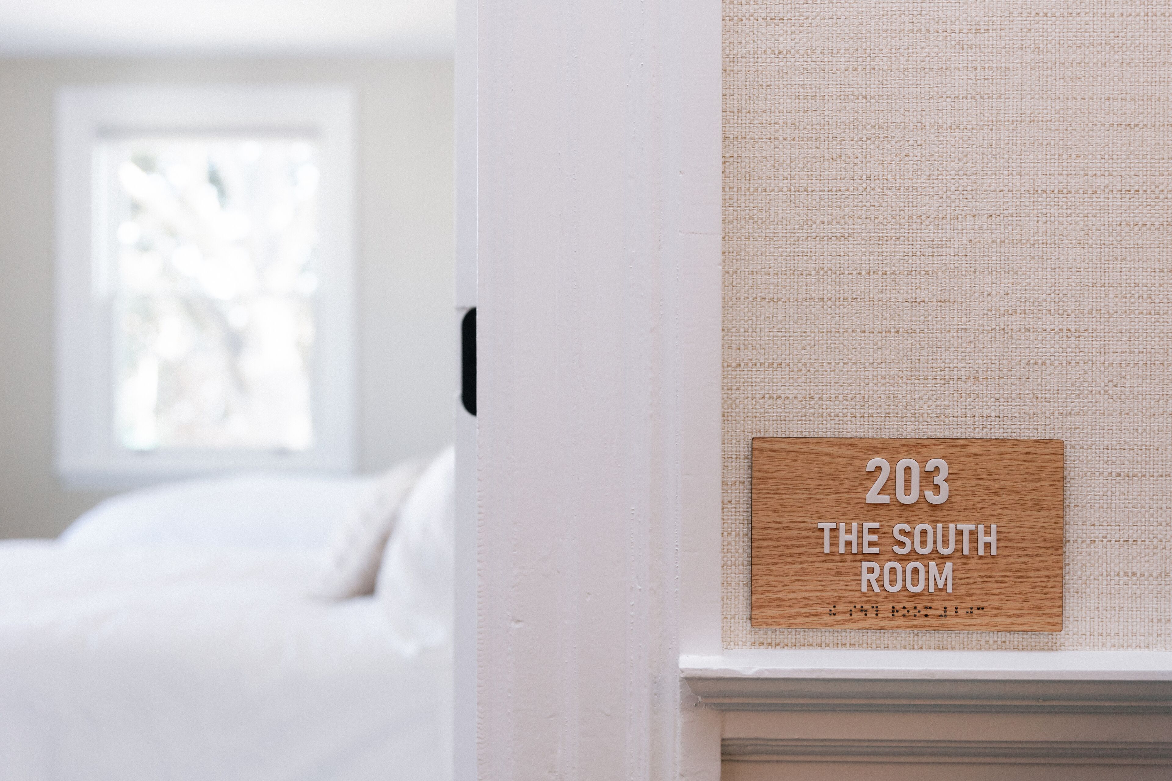 A sign indicating room number 203, labeled as "The South Room," mounted on a textured wall near a window.
