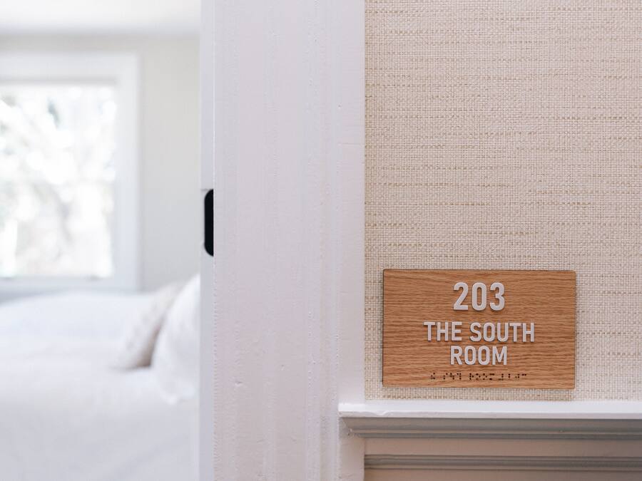 A sign indicating room number 203, labeled as "The South Room," mounted on a textured wall near a window.