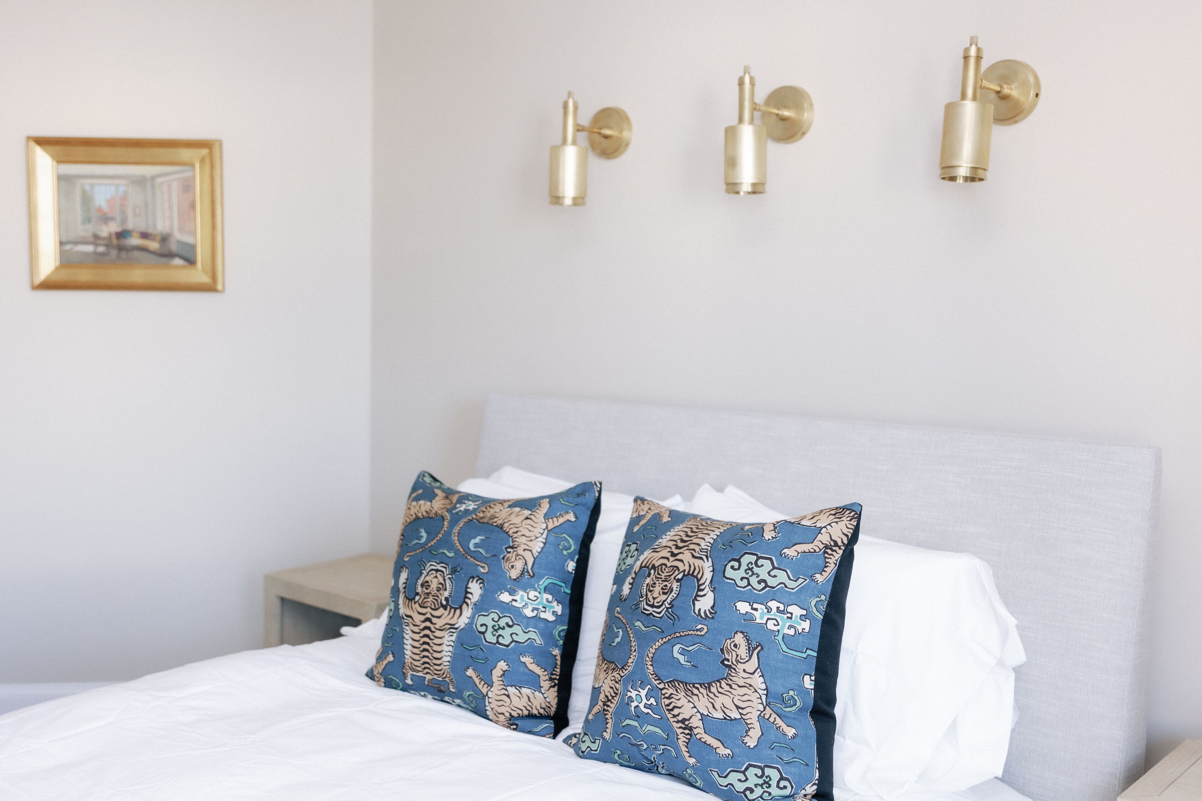 Una cama bien hecha con sábanas blancas y dos almohadas decorativas con estampado de tigre azul y dorado.