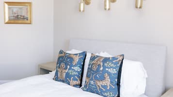 A neatly made bed with white linens and two decorative pillows featuring a blue and gold tiger pattern.