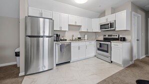 A modern kitchen with white cabinets, stainless steel appliances, and a tiled floor. - The Bell Inn (Peabody)
