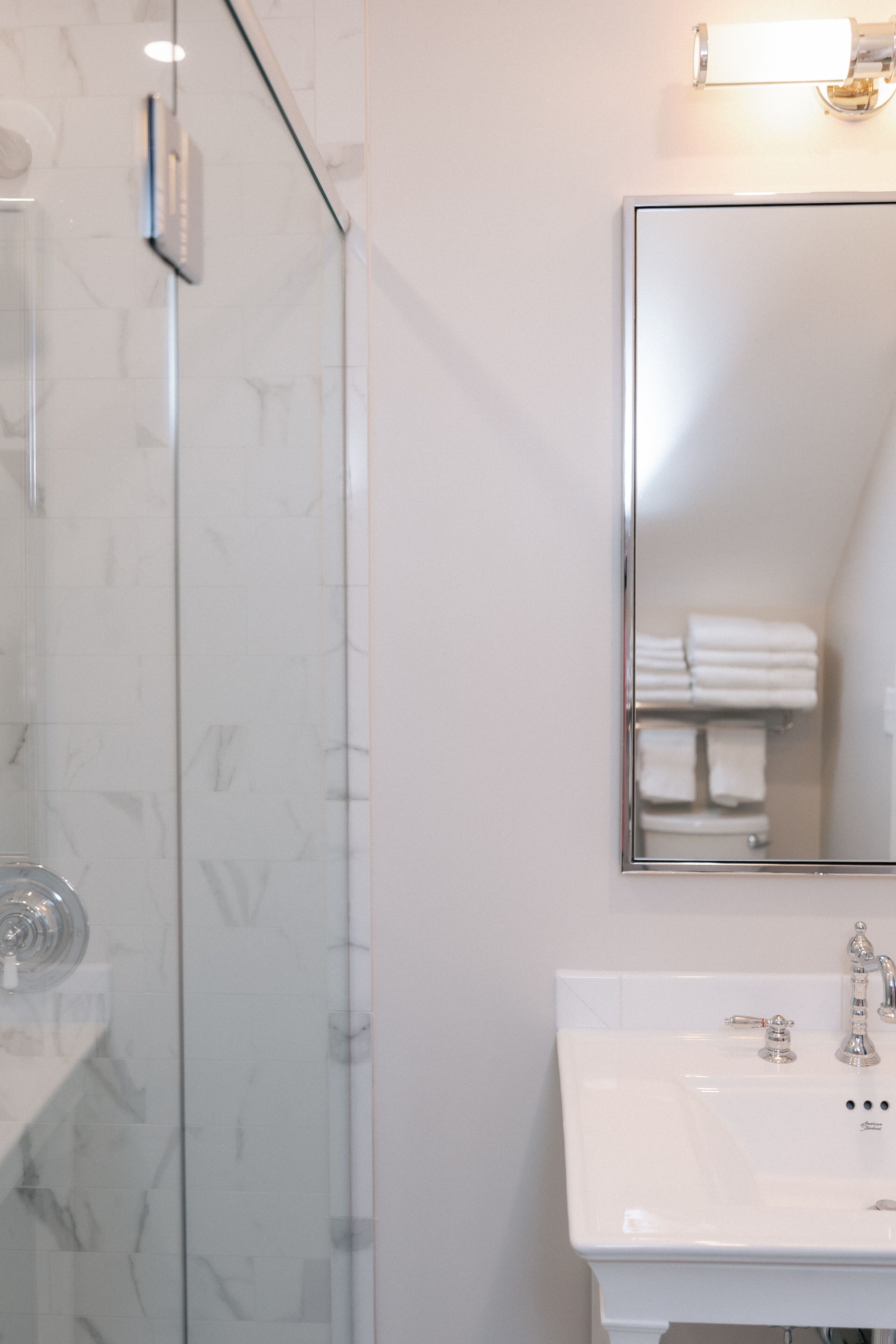 A bathroom with a glass shower enclosure, a white sink with a mirror above it, and a towel rack with folded towels.